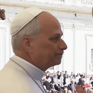 A Man Wearing A White Hat Is Standing In Front Of A Crowd Of People GIF