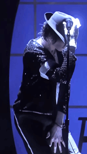A Man Wearing A White Hat Is Standing In Front Of A Microphone GIF