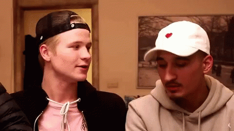 A Man Wearing A White Hat With A Red Heart On It Is Talking To Another Man . GIF