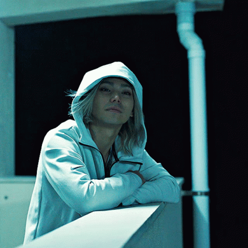 A Man Wearing A White Hoodie Is Leaning On A Railing With His Arms Crossed GIF