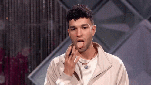 A Man Wearing A White Jacket And A Necklace Is Sticking His Tongue Out . GIF