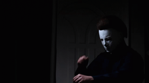 a man wearing a white mask is standing in a dark room