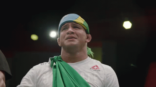 A Man Wearing A White Reebok Shirt With A Green Cloth Around His Neck GIF