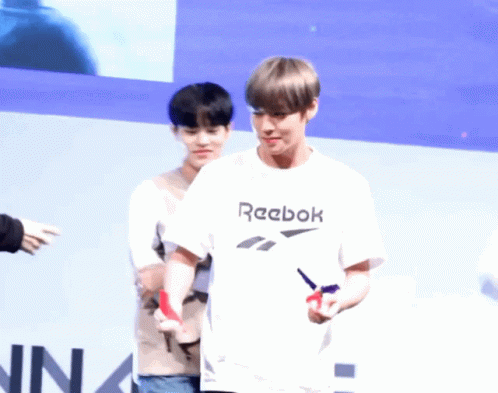 A Man Wearing A White Reebok T-Shirt Stands Next To Another Person GIF