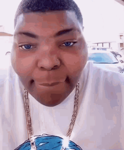 A Man Wearing A White Shirt And A Gold Chain Is Making A Face . GIF