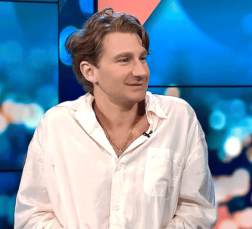 A Man Wearing A White Shirt And A Necklace Smiles GIF