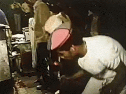 A Man Wearing A White Shirt And A Red Hat Is Kneeling Down In A Dark Room . GIF