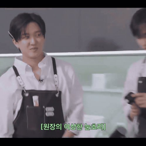 A Man Wearing A White Shirt And Black Apron Is Talking To Another Man GIF
