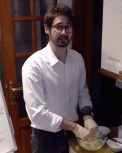 A Man Wearing A White Shirt And Gloves Is Preparing Food In A Kitchen GIF