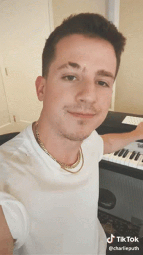 A Man Wearing A White Shirt And Gold Chain Is Standing In Front Of A Keyboard .. GIF