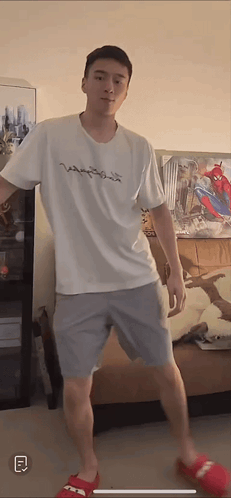 A Man Wearing A White Shirt And Grey Shorts Is Standing In A Living Room GIF
