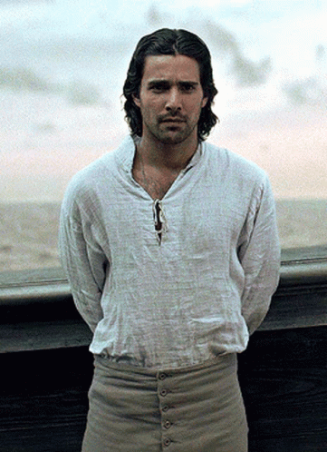 A Man Wearing A White Shirt And Khaki Pants Stands In Front Of A Window GIF