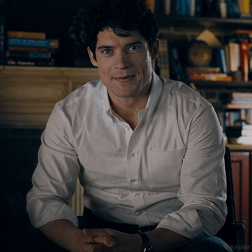 A Man Wearing A White Shirt Is Sitting In A Chair GIF