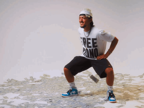 A Man Wearing A White Shirt That Says Free Dino Is Squatting In Front Of A Pile Of Money GIF