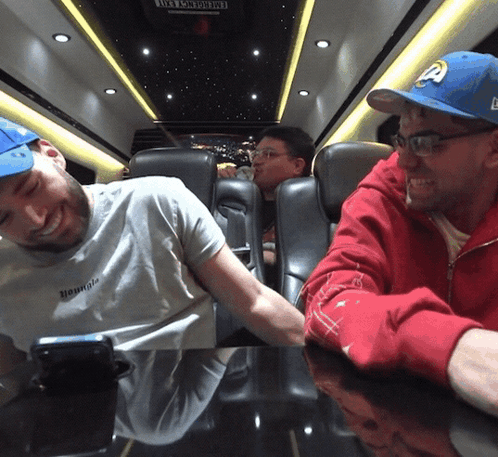 A Man Wearing A White Shirt That Says " Hounds " Sits Next To Another Man GIF