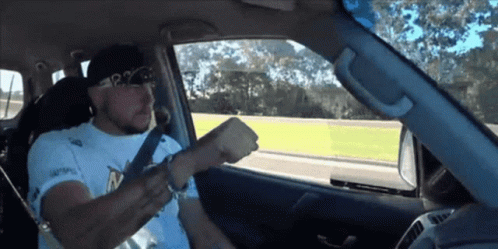 A Man Wearing A White Shirt That Says P2 On It Is Driving A Car GIF