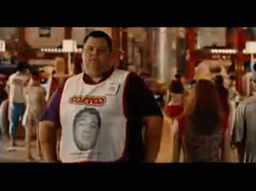 A Man Wearing A White Shirt With A Picture Of A Man On It Is Standing In A Crowded Room . GIF