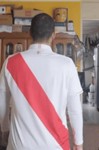 A Man Wearing A White Shirt With A Red Stripe On The Back Is Standing In A Living Room . GIF