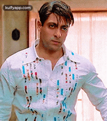 A Man Wearing A White Shirt With Paint Splattered On It Is Standing In Front Of A Window . GIF