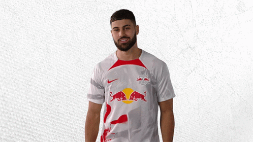 a man wearing a white shirt with red bulls on it is waving