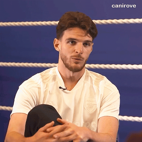 A Man Wearing A White Shirt With The Word Arsenal On It Sits In A Boxing Ring GIF