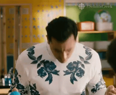 A Man Wearing A White Sweater With Blue Flowers On It Is Standing In A Kitchen GIF