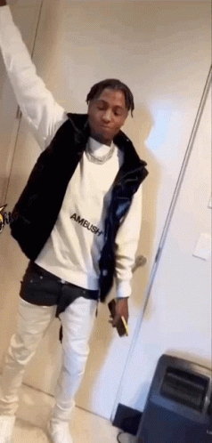 A Man Wearing A White Sweatshirt And A Black Vest Is Standing In A Room With His Arms In The Air . GIF