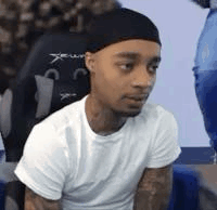 A Man Wearing A White T-Shirt And A Black Headband Is Sitting In A Chair . GIF