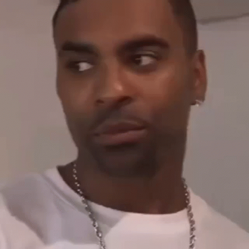 A Man Wearing A White T-Shirt And A Necklace Is Making A Funny Face . GIF