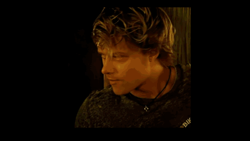 A Man Wearing A White T-Shirt Is Sitting In Front Of A Window Holding A Pair Of Gloves . GIF