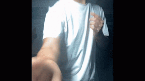 A Man Wearing A White T-Shirt Is Standing In The Dark GIF