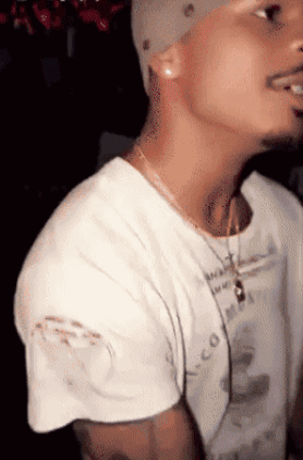 A Man Wearing A White T-Shirt With A Necklace Around His Neck And A Hat On GIF
