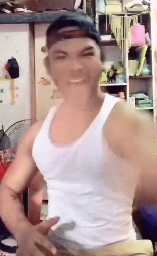 a man wearing a white tank top and a hat is making a funny face