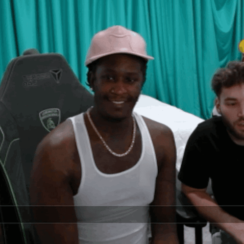 A Man Wearing A White Tank Top And A Pink Hat Has A Lamborghini Logo On His Chair GIF