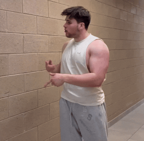 A Man Wearing A White Tank Top And Grey Shorts With The Letter S On The Bottom GIF