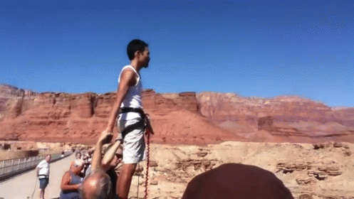 A Man Wearing A White Tank Top And Shorts Is Standing In Front Of A Desert Landscape GIF
