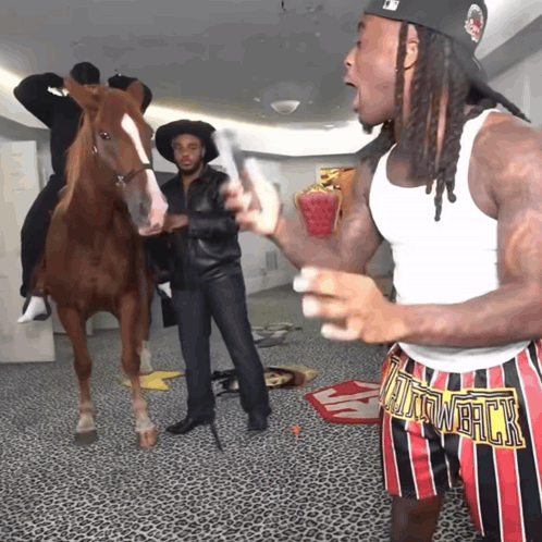 A Man Wearing A White Tank Top And Shorts That Say ' Tain Whack ' Stands In Front Of A Horse GIF
