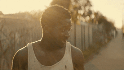 A Man Wearing A White Tank Top Is Walking Down A Road GIF