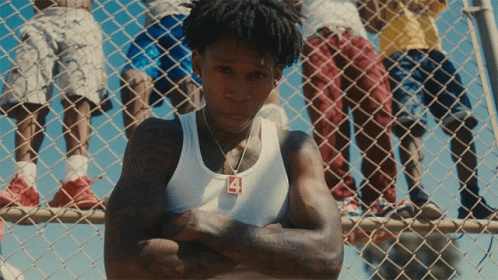 A Man Wearing A White Tank Top With The Number 4 On It Stands In Front Of A Chain Link Fence GIF