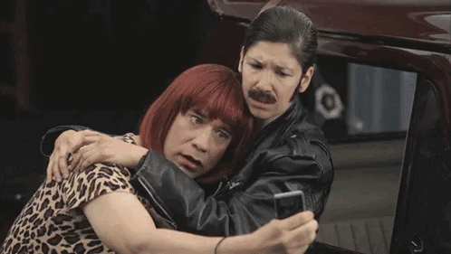 A Man Wearing A Wig And A Leather Jacket Is Standing Next To Another Man Wearing A Leather Jacket . GIF