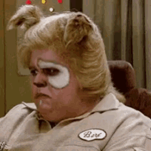 A Man Wearing A Wig And A Patch On His Shirt Is Sitting In A Chair With His Face Painted Like A Dog . GIF