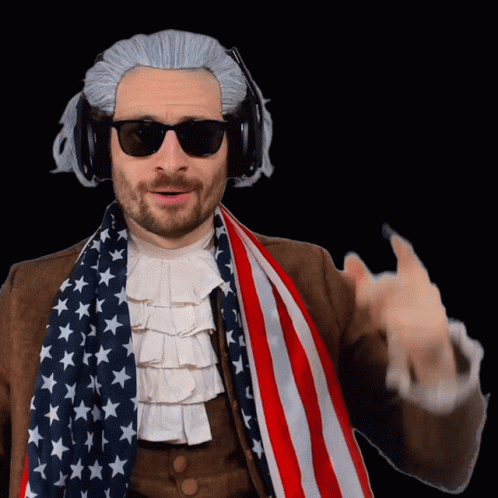 A Man Wearing A Wig And Sunglasses Holds An American Flag Around His Neck GIF
