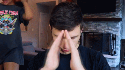 A Man Wearing A World Tour T-Shirt Is Covering His Face With His Hands GIF