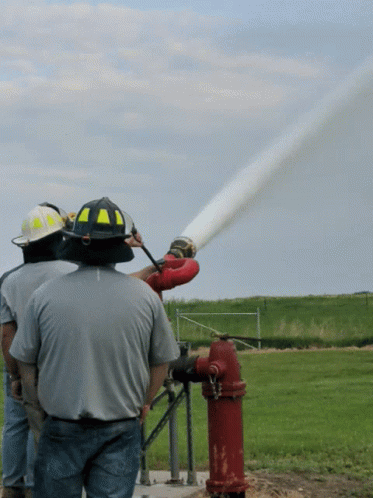 A Man Wearing A Yellow And Black Helmet Is Spraying Water From A Fire Hydrant GIF