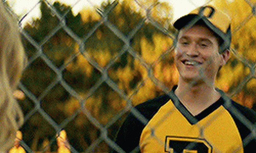 A Man Wearing A Yellow And Black Jersey With The Letter P On It Is Smiling Behind A Chain Link Fence . GIF