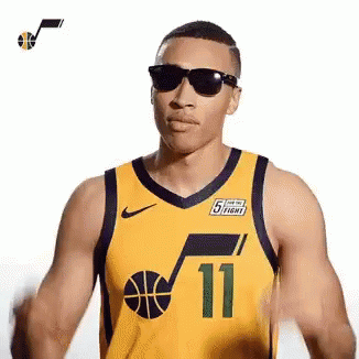 A Man Wearing A Yellow Basketball Jersey And Sunglasses Is Standing In Front Of A White Background . GIF