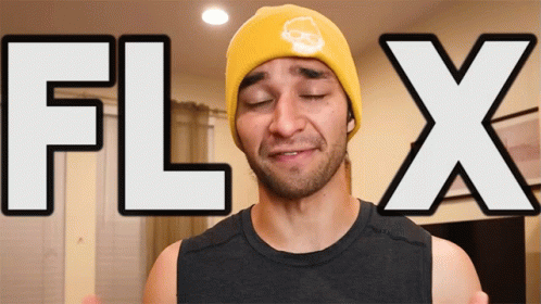 A Man Wearing A Yellow Beanie With A Skull On It Stands In Front Of A Sign That Says Flix GIF