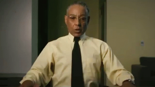 A Man Wearing A Yellow Shirt And A Black Tie Is Sitting At A Table . GIF