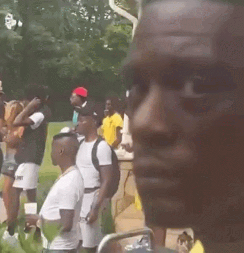 A Man Wearing A Yellow Shirt And A Gold Chain Is Standing In Front Of A Crowd Of People . GIF