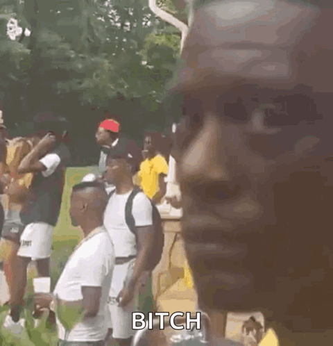 A Man Wearing A Yellow Shirt And A Necklace Is Standing In Front Of A Group Of People . GIF